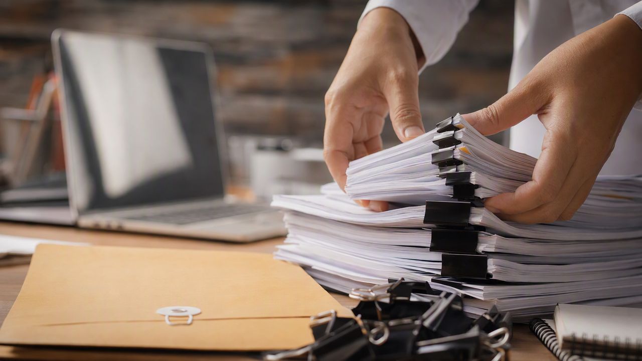 Hands arranging a document production beside a laptop with the screen out of focus.